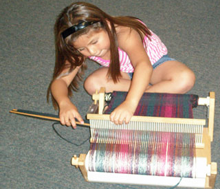 Photo of a girl learning to weave on a rigid heddle loom